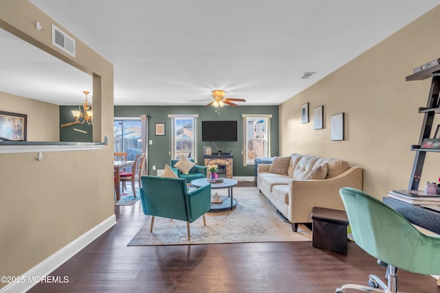 living room with ceiling fan with notable chandelier, wood finished floors, visible vents, and baseboards