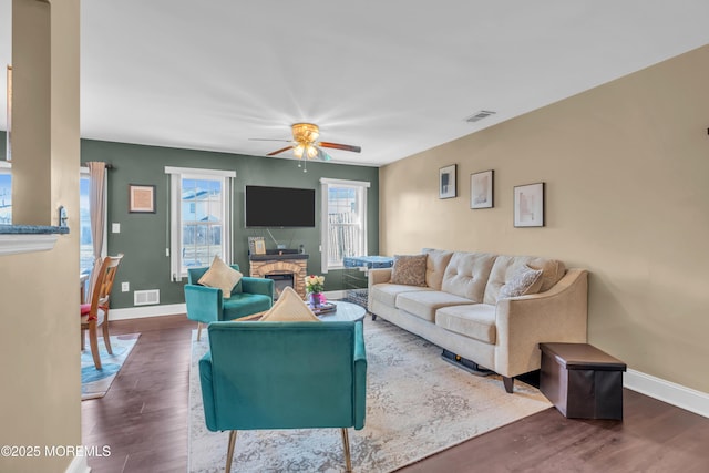 living area featuring a stone fireplace, wood finished floors, visible vents, and baseboards