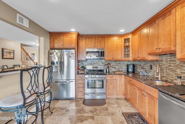 kitchen with stainless steel appliances, a sink, visible vents, dark stone counters, and tasteful backsplash