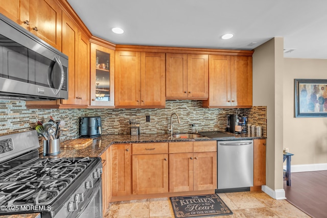 kitchen featuring tasteful backsplash, glass insert cabinets, dark stone countertops, stainless steel appliances, and a sink