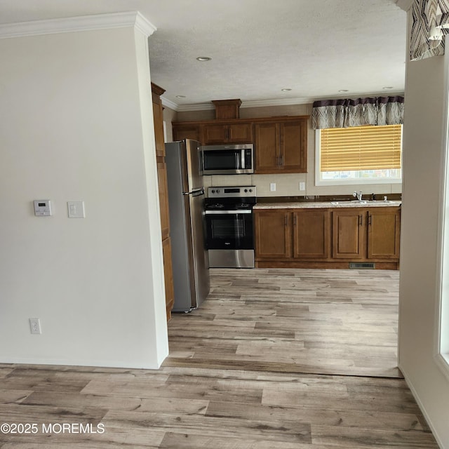 kitchen featuring light wood-type flooring, appliances with stainless steel finishes, a sink, and ornamental molding