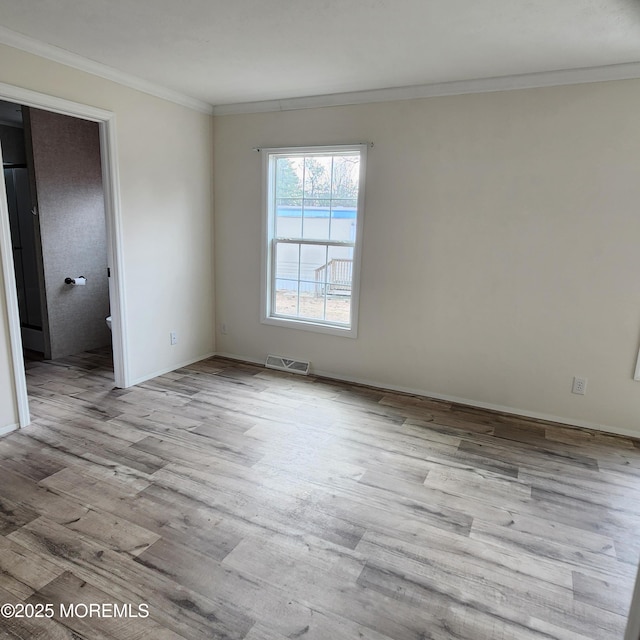 spare room featuring visible vents, crown molding, baseboards, and wood finished floors