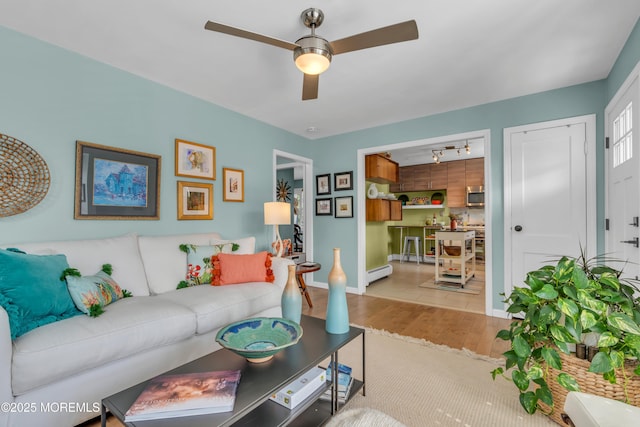 living area featuring ceiling fan, a baseboard radiator, wood finished floors, and baseboards