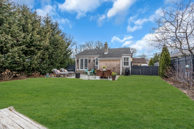 rear view of house with french doors, a chimney, a lawn, a patio area, and a fenced backyard