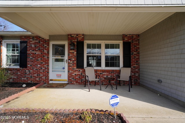 doorway to property with a porch and brick siding