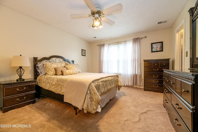 bedroom with a textured ceiling, ceiling fan, visible vents, and light colored carpet