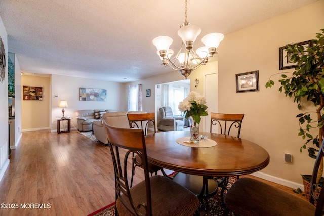 dining space with a notable chandelier, a textured ceiling, baseboards, and wood finished floors