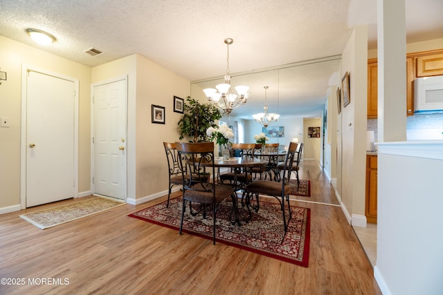 dining space with light wood finished floors, baseboards, visible vents, a textured ceiling, and a chandelier