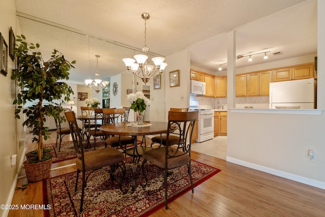 dining space with a notable chandelier, visible vents, light wood-style floors, a textured ceiling, and baseboards