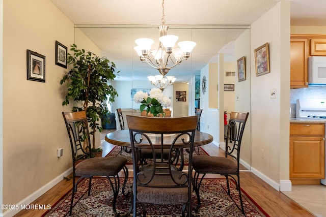 dining area with a chandelier, baseboards, and light wood finished floors