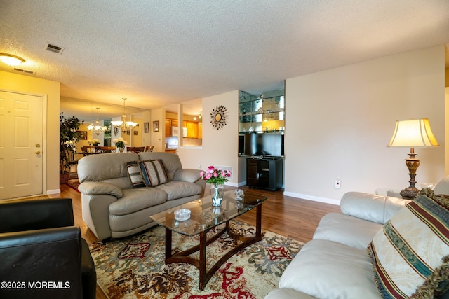 living room featuring visible vents, a textured ceiling, wood finished floors, a chandelier, and baseboards