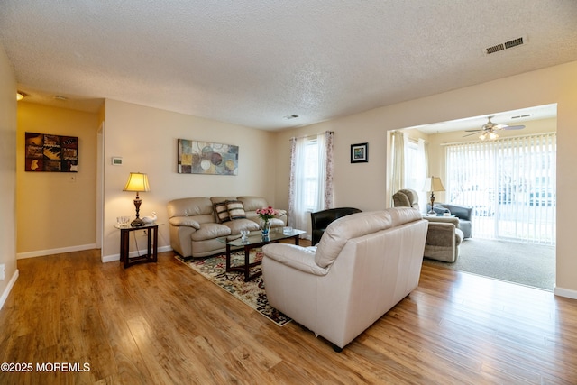 living area with a textured ceiling, a wealth of natural light, light wood-style flooring, and visible vents