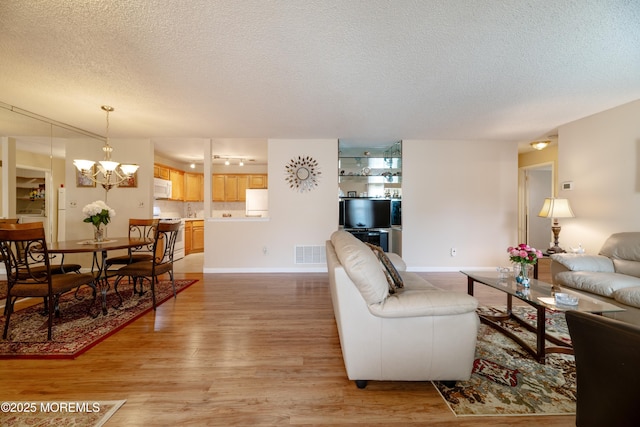 living area featuring visible vents, a textured ceiling, a chandelier, light wood-type flooring, and baseboards