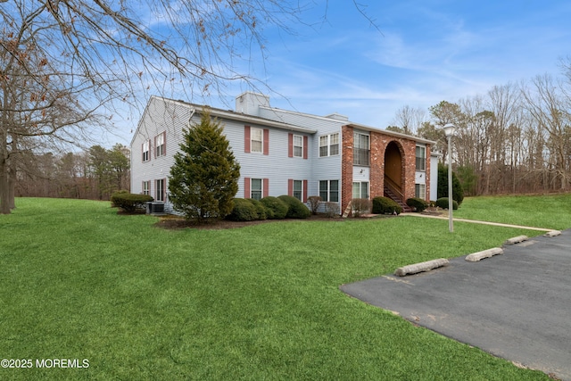 view of front of house featuring a front lawn, a chimney, central AC unit, and brick siding