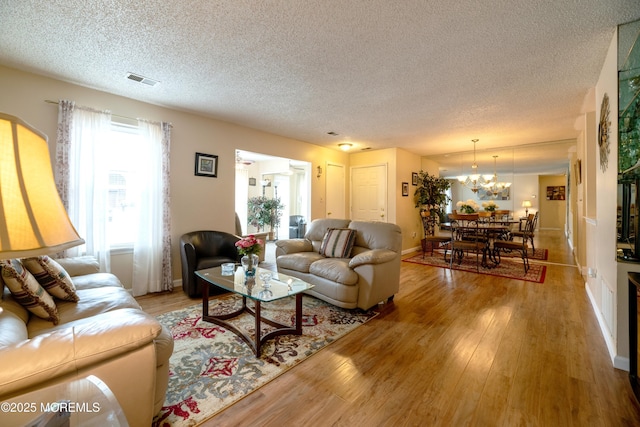 living room featuring a notable chandelier, a textured ceiling, visible vents, and wood finished floors