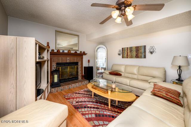 living room with a textured ceiling, ceiling fan, a glass covered fireplace, and wood finished floors