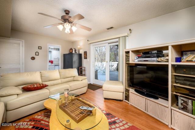 living area featuring light wood-style floors, a textured ceiling, visible vents, and a ceiling fan