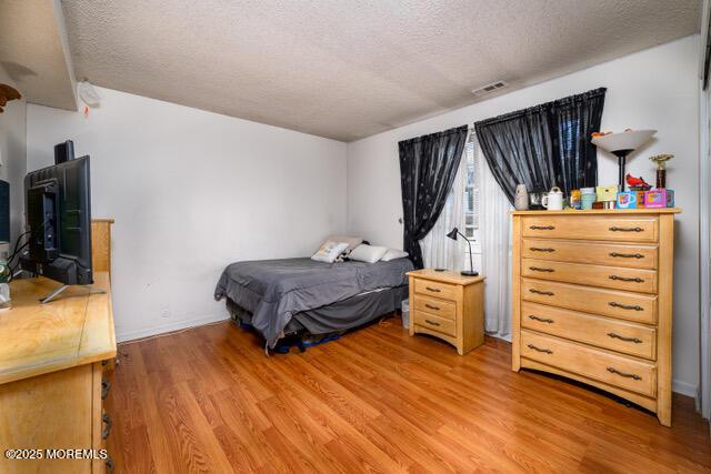 bedroom featuring light wood-type flooring, visible vents, a textured ceiling, and baseboards