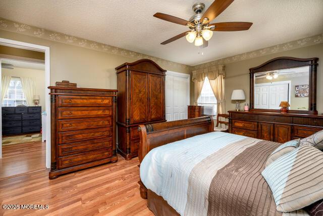 bedroom with a textured ceiling, ceiling fan, multiple windows, and light wood-type flooring