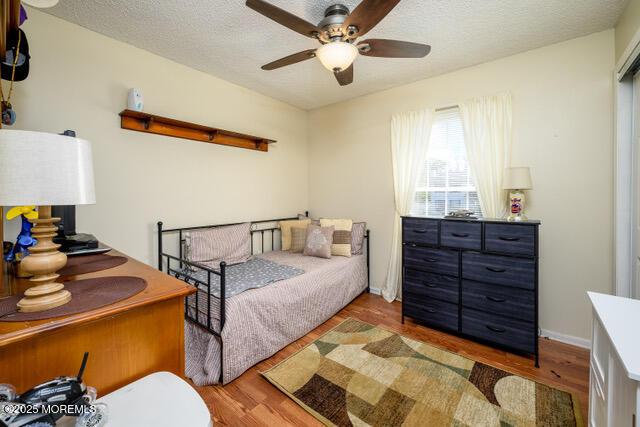 bedroom with a textured ceiling, ceiling fan, wood finished floors, and baseboards