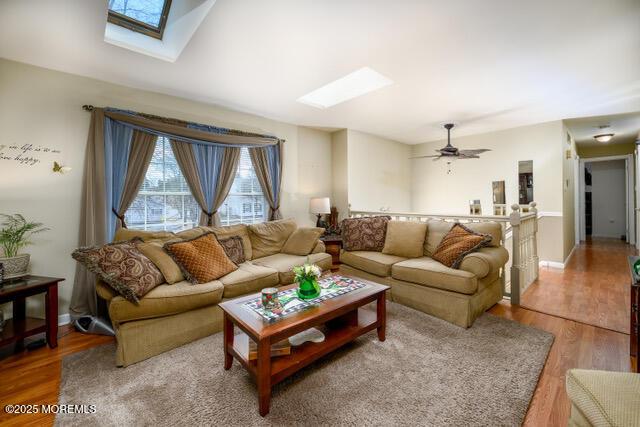 living area featuring light wood-type flooring, a skylight, and baseboards