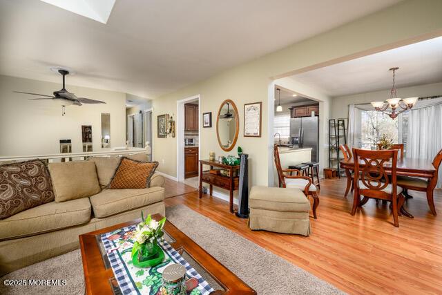 living area with ceiling fan with notable chandelier and light wood-style floors