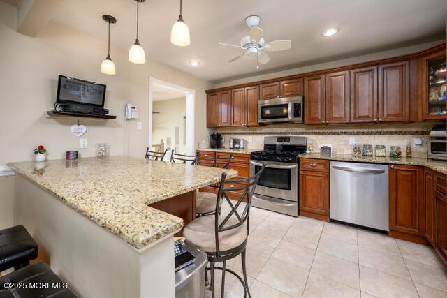 kitchen featuring light stone counters, a breakfast bar area, stainless steel appliances, a peninsula, and backsplash