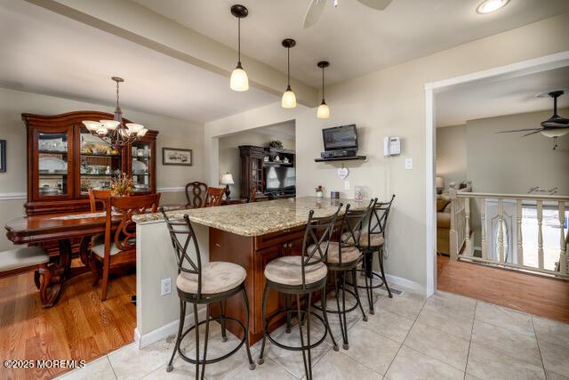 kitchen featuring ceiling fan with notable chandelier, hanging light fixtures, light tile patterned floors, and a breakfast bar area