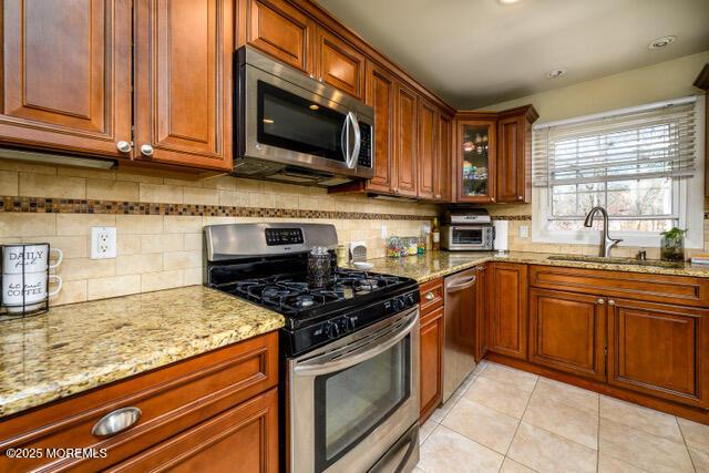 kitchen with light tile patterned floors, tasteful backsplash, light stone counters, stainless steel appliances, and a sink