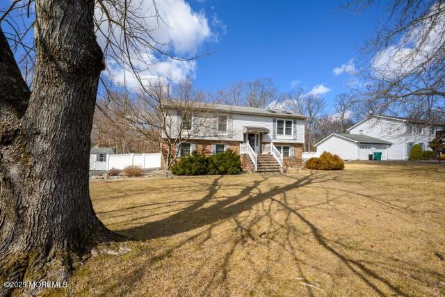 split foyer home featuring brick siding, fence, and a front lawn