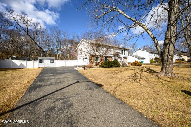 view of front of home featuring aphalt driveway, an outbuilding, fence, and a front lawn