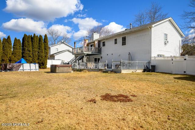 back of house with a yard, a fenced backyard, a wooden deck, and a hot tub