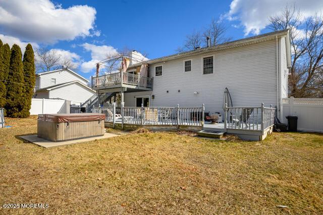 rear view of house with a balcony, a hot tub, a fenced backyard, and a yard