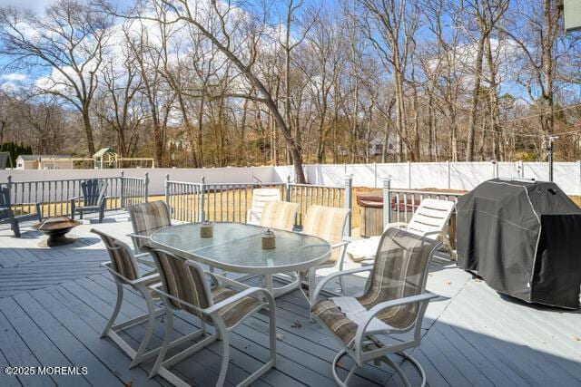 deck featuring outdoor dining space, a fenced backyard, a playground, and a grill