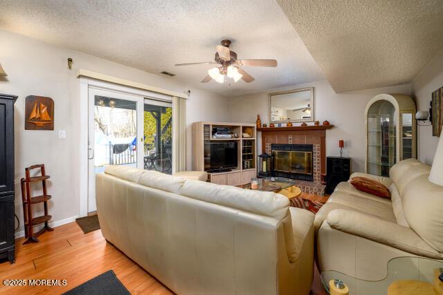 living area with a textured ceiling, a ceiling fan, baseboards, light wood-style floors, and a glass covered fireplace