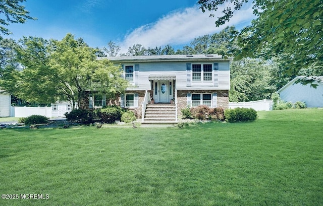 raised ranch featuring brick siding, fence, and a front yard