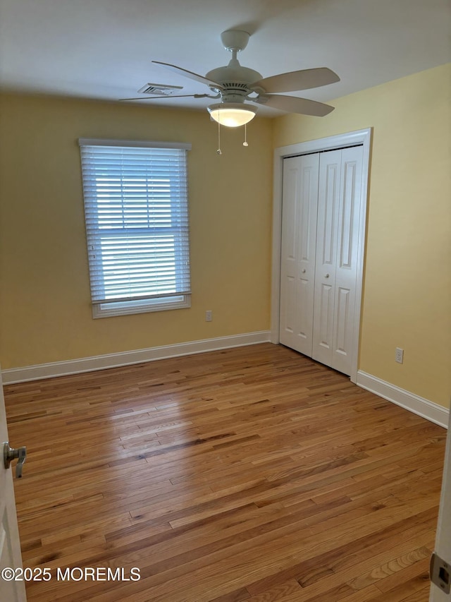 unfurnished bedroom featuring a ceiling fan, visible vents, wood finished floors, baseboards, and a closet