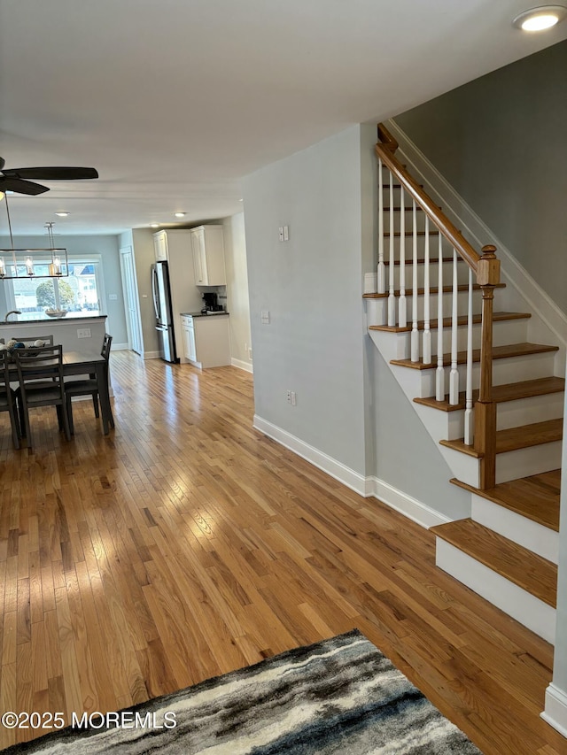 unfurnished living room featuring light wood-type flooring, stairway, baseboards, and a ceiling fan