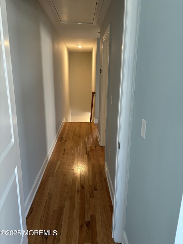 hall featuring an upstairs landing, attic access, baseboards, and hardwood / wood-style floors