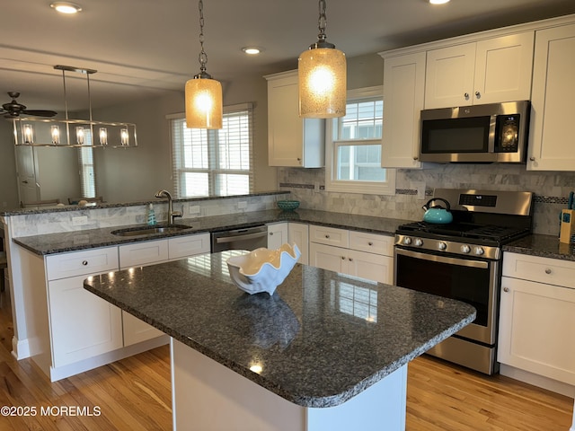 kitchen with a sink, stainless steel appliances, light wood-style floors, a peninsula, and a healthy amount of sunlight