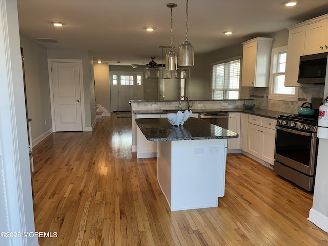 kitchen with white cabinets, appliances with stainless steel finishes, light wood-style flooring, and a peninsula