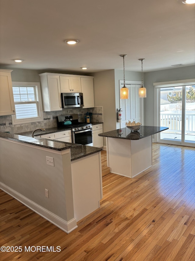 kitchen featuring decorative backsplash, light wood-style flooring, dark stone countertops, white cabinets, and stainless steel appliances