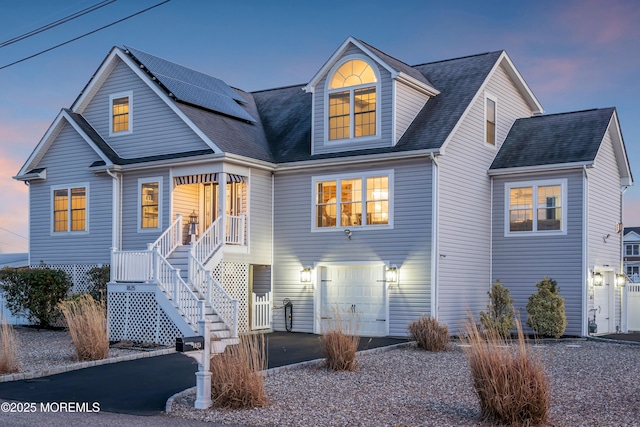 view of front facade with aphalt driveway, a porch, a garage, stairs, and roof mounted solar panels