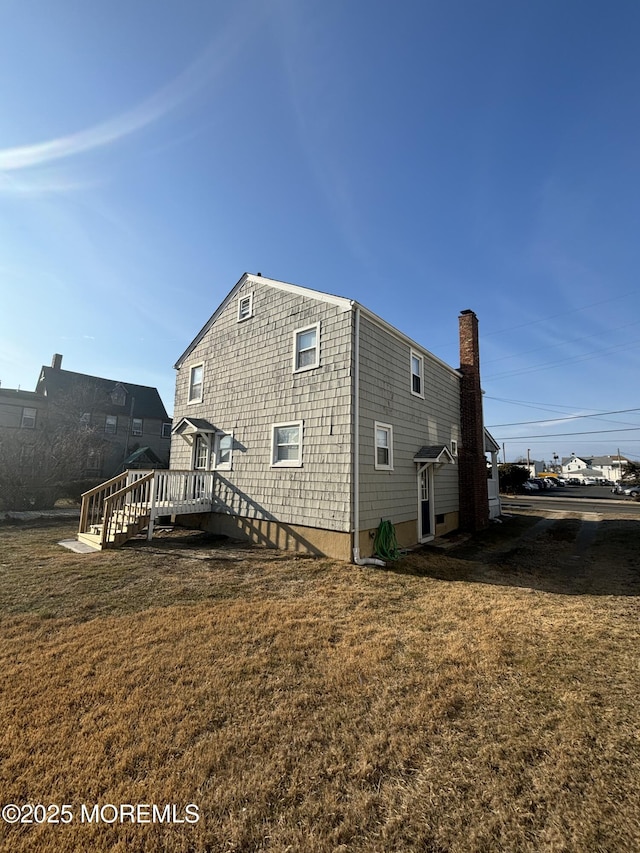 rear view of house with a chimney, a lawn, and a wooden deck