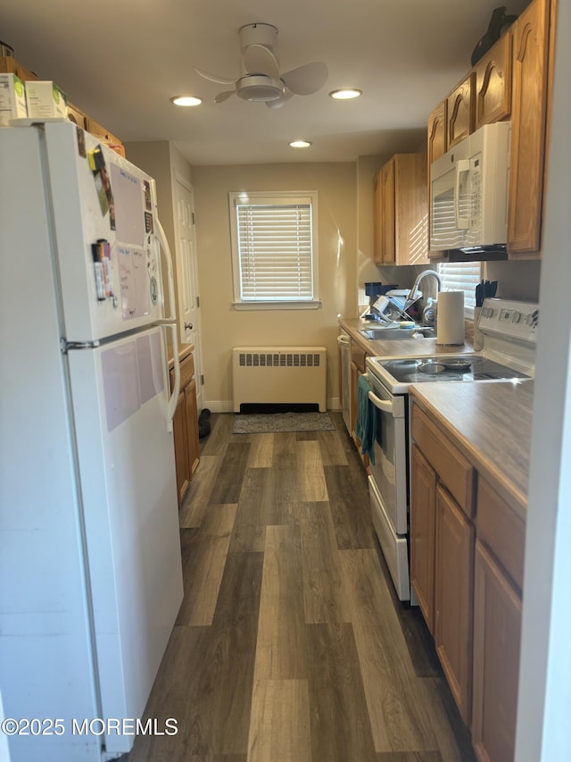 kitchen featuring dark wood finished floors, radiator, a sink, ceiling fan, and white appliances