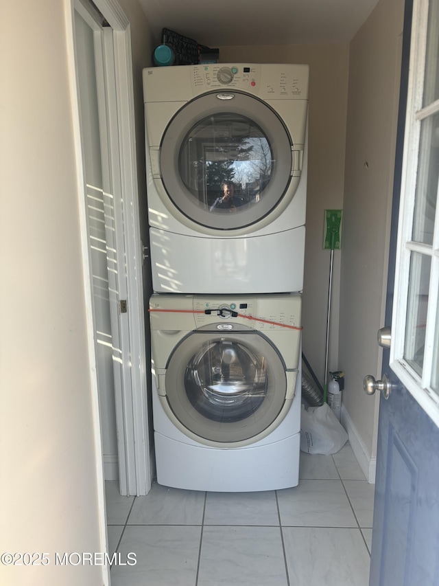 clothes washing area featuring stacked washing maching and dryer, baseboards, and laundry area