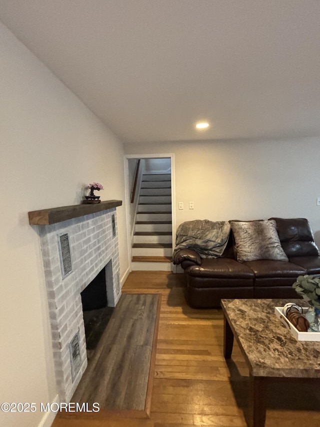 living area featuring a brick fireplace, stairs, visible vents, and wood finished floors