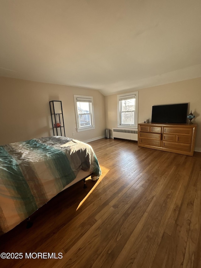 bedroom with vaulted ceiling, wood finished floors, and radiator