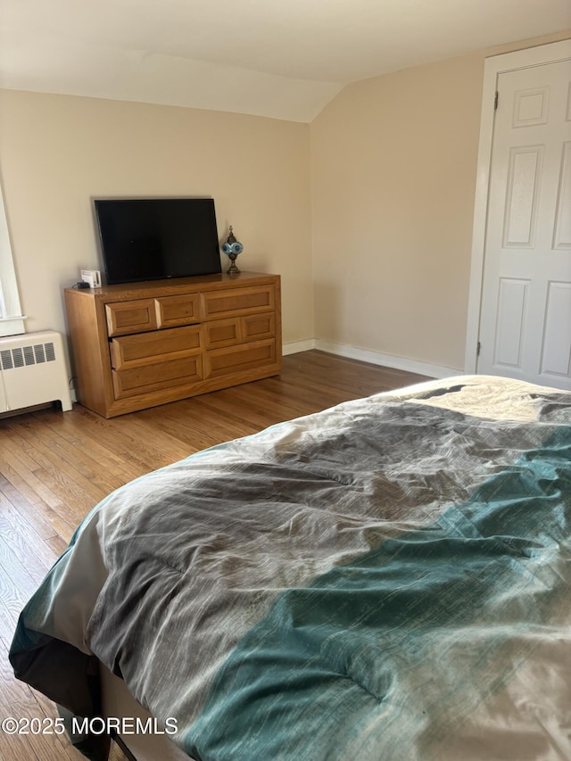 bedroom featuring radiator, vaulted ceiling, baseboards, and wood finished floors