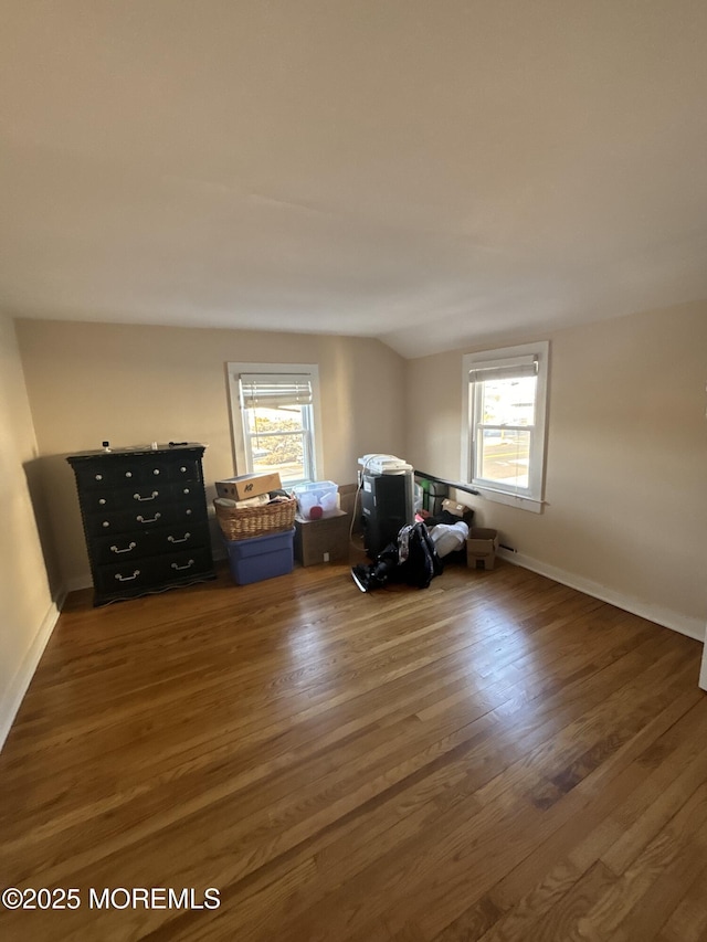 interior space with a healthy amount of sunlight, vaulted ceiling, baseboards, and wood finished floors